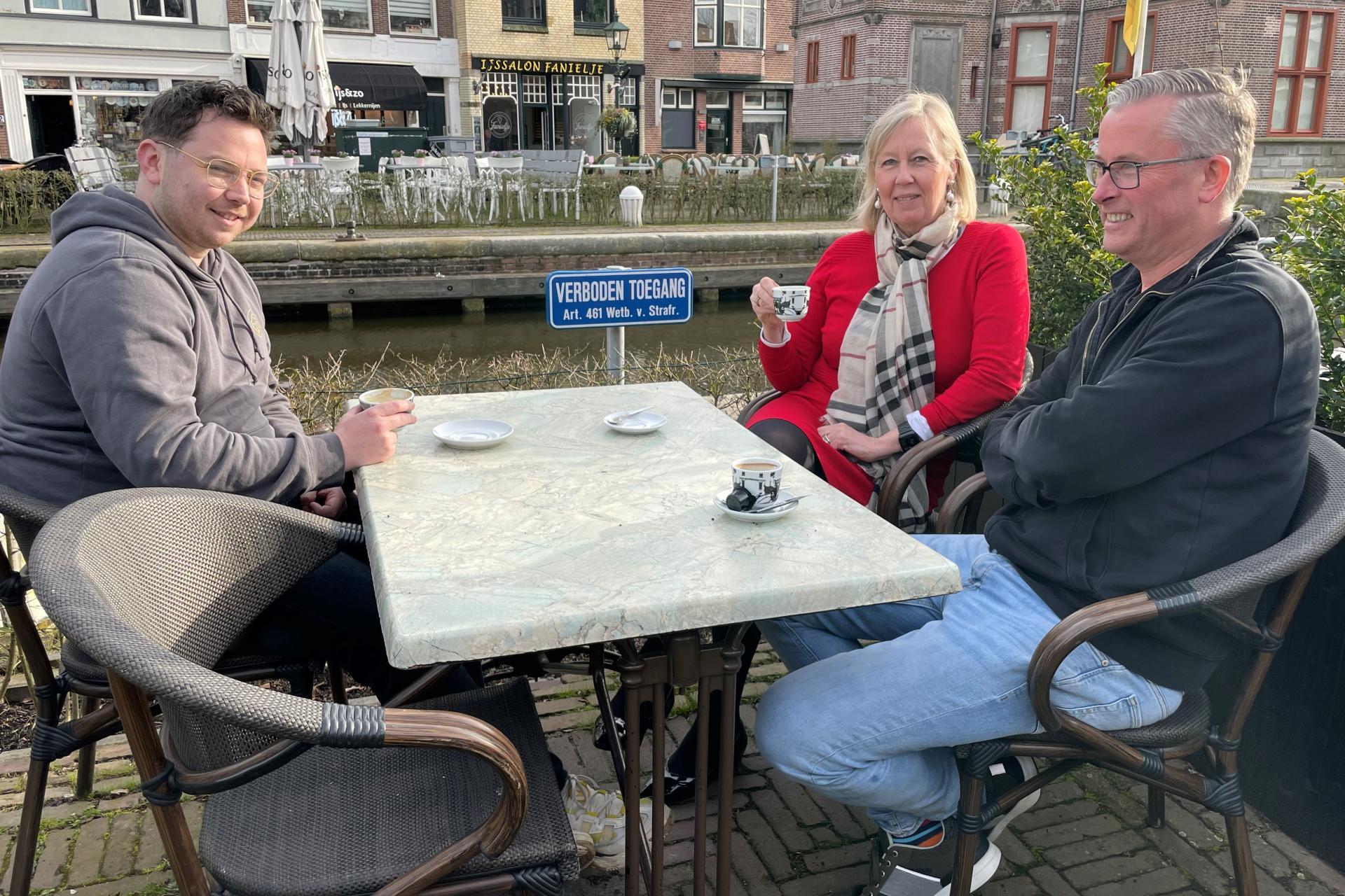 Op een terras bij de sluis van Leidschendam drinkt wethouder Astrid van Eekelen koffie met Alfred van Kesteren, voorzitter van ondernemersfonds Leidschendam-Centrum, en Jim den Harder van restaurant Old Fashion.